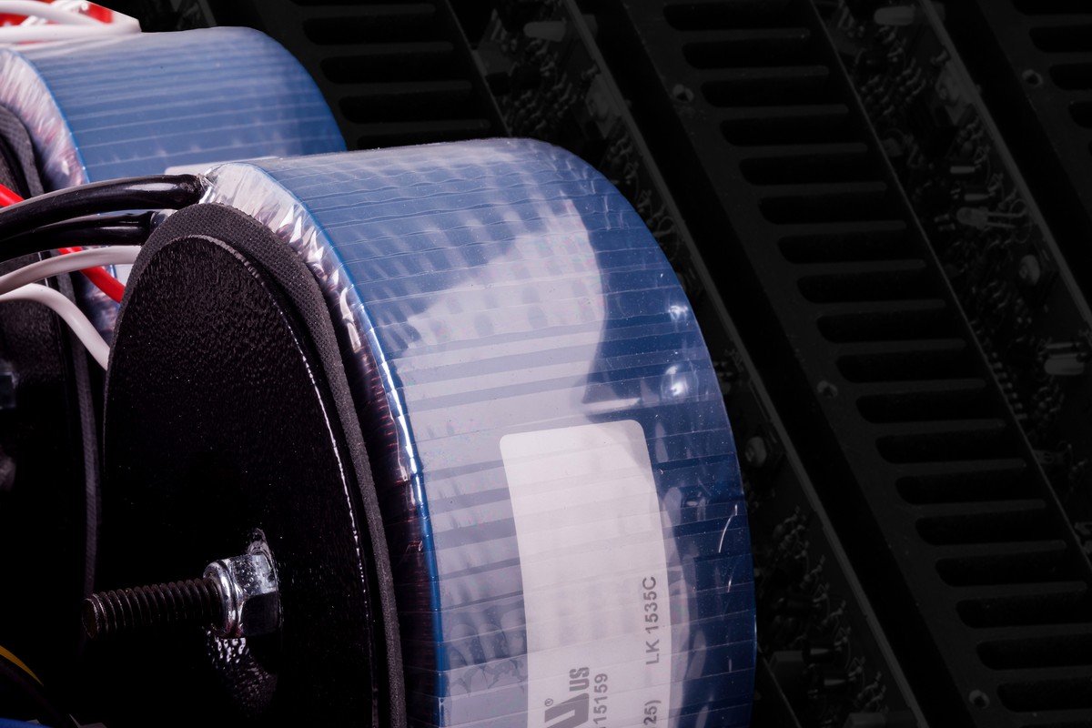 Close-up of toroidal transformers wrapped in blue tape in front of aluminium heatsinks