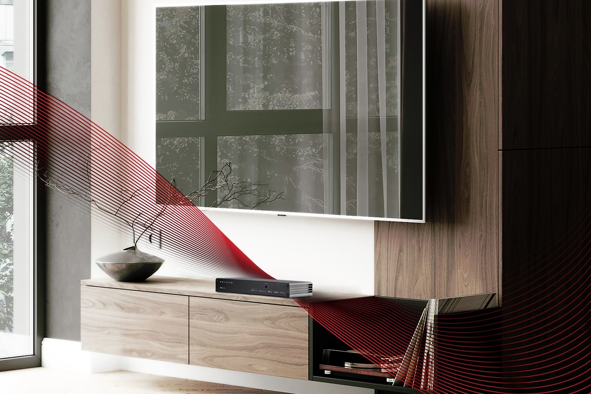Wandmontierter Fernseher über einem niedrigen Holzschrank, mit dem kompakten Receiver auf dem Schrank und einem stilisierten roten Band