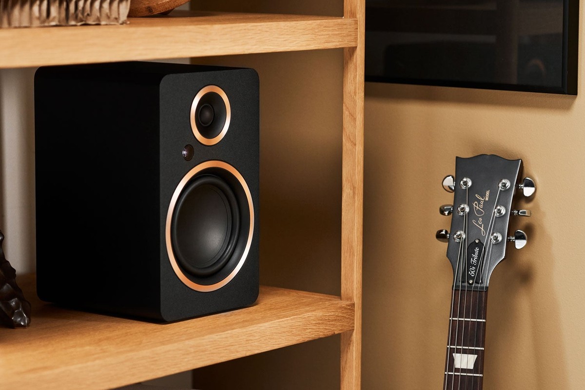 Diffusore nero su una mensola in legno accanto a una chitarra elettrica