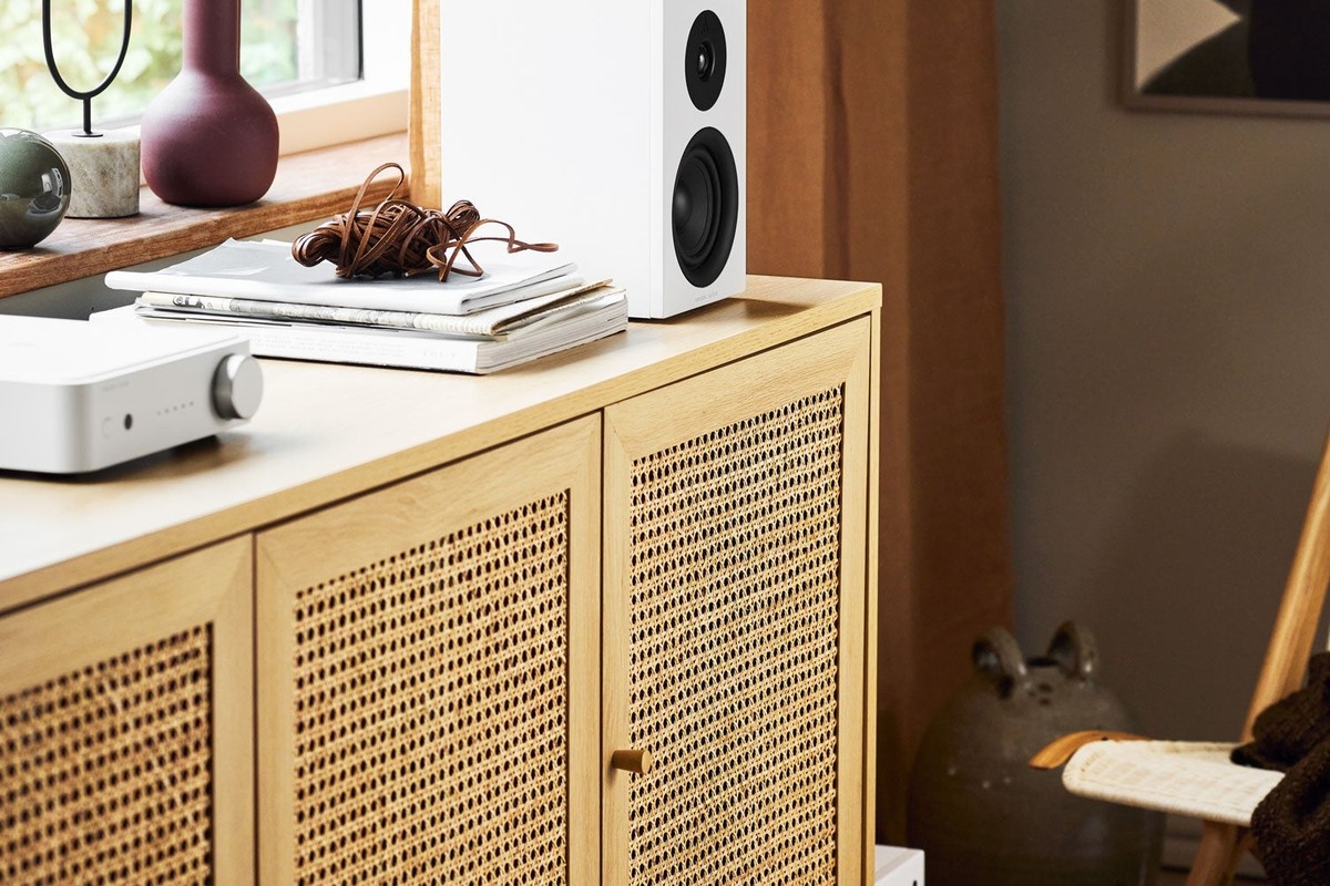 Credenza in rattan con un amplificatore bianco, un diffusore bianco e un subwoofer a terra