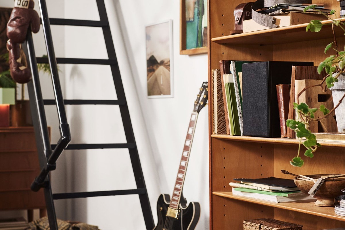 Libreria in legno accanto a una scala e a una chitarra, con un diffusore nero sul ripiano alto