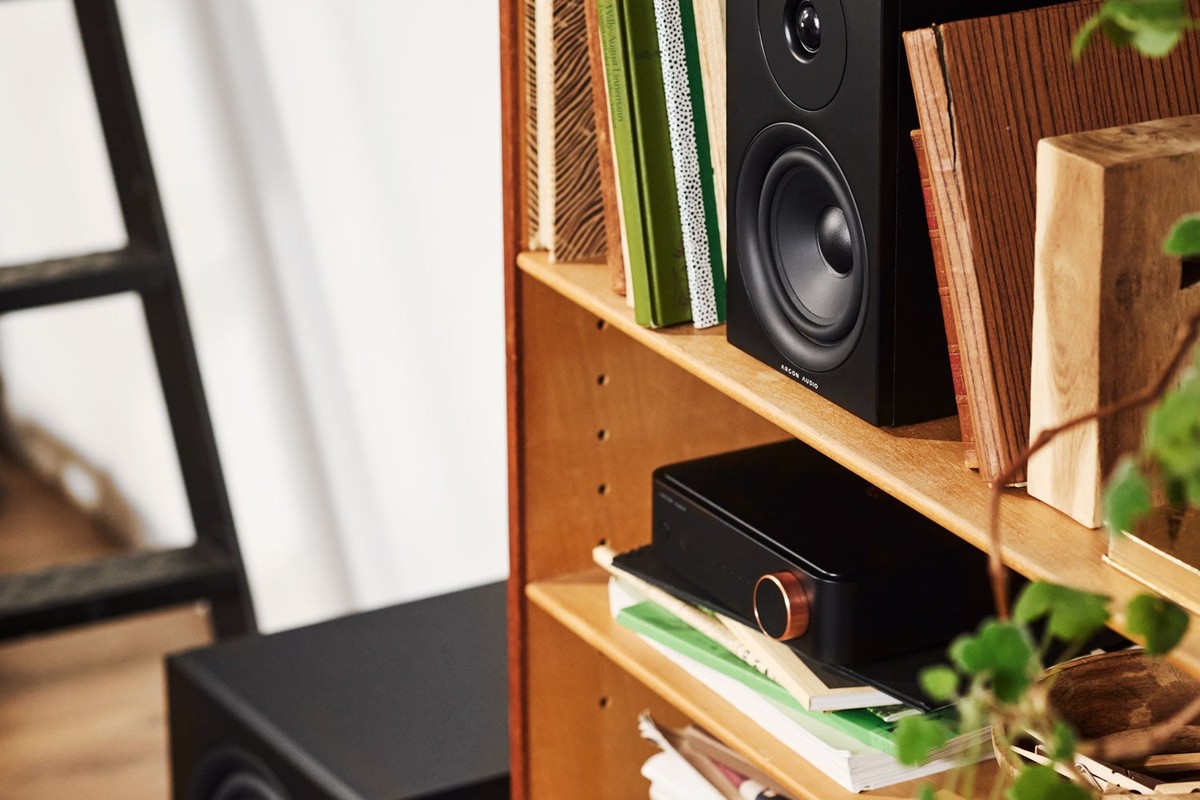 Diffusore nero su una mensola sopra un amplificatore, con un subwoofer a terra
