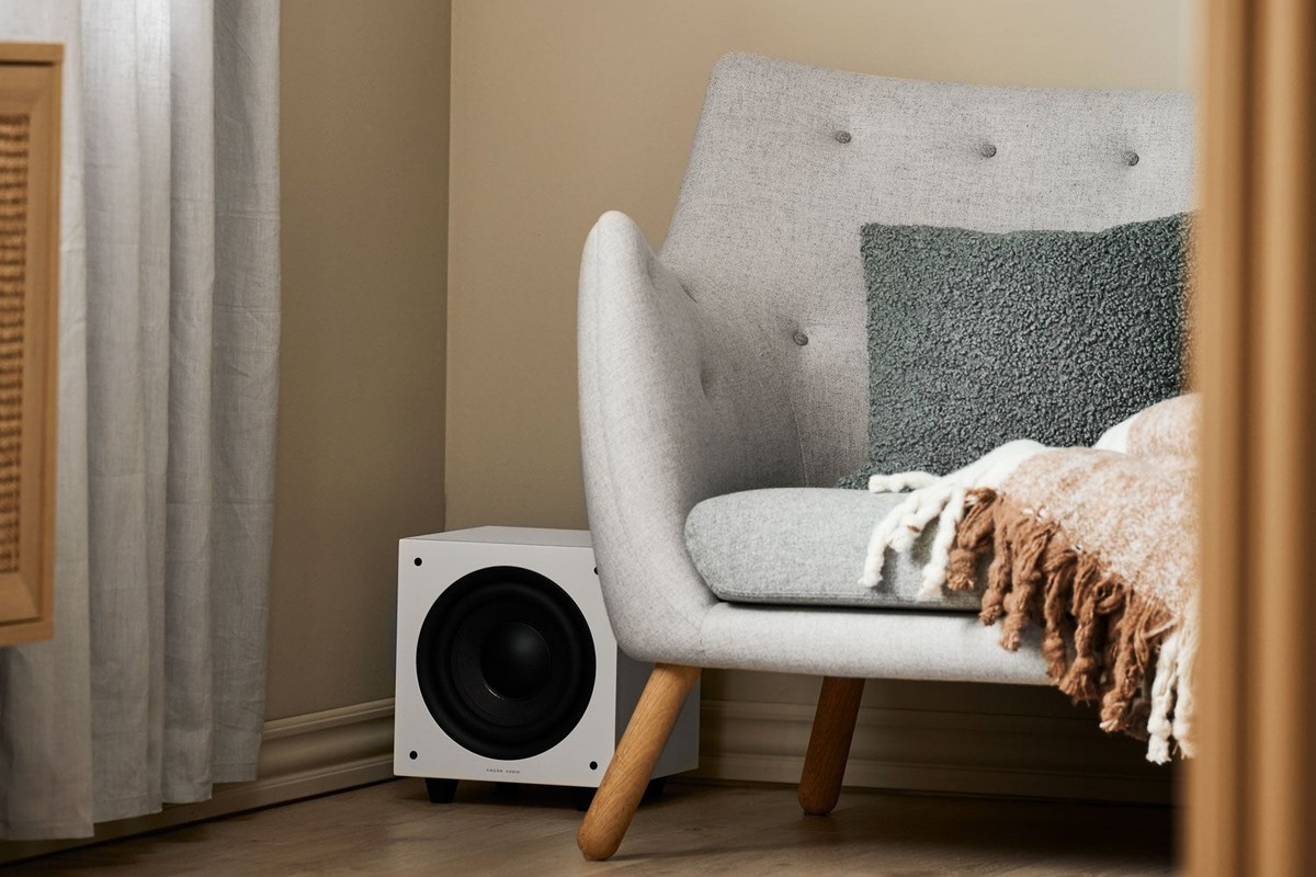 Bright living room with white wall speakers and a small white subwoofer on the floor