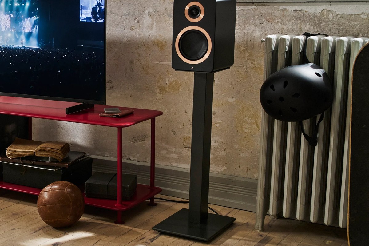 Black speaker on a steel stand in a living room, next to a red TV cabinet