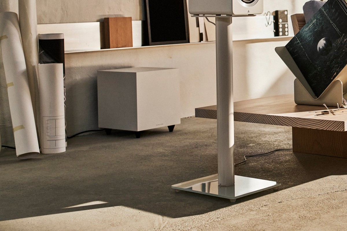 Mattweisser Subwoofer auf dem Wohnzimmerboden neben einem Lautsprecher auf Ständer