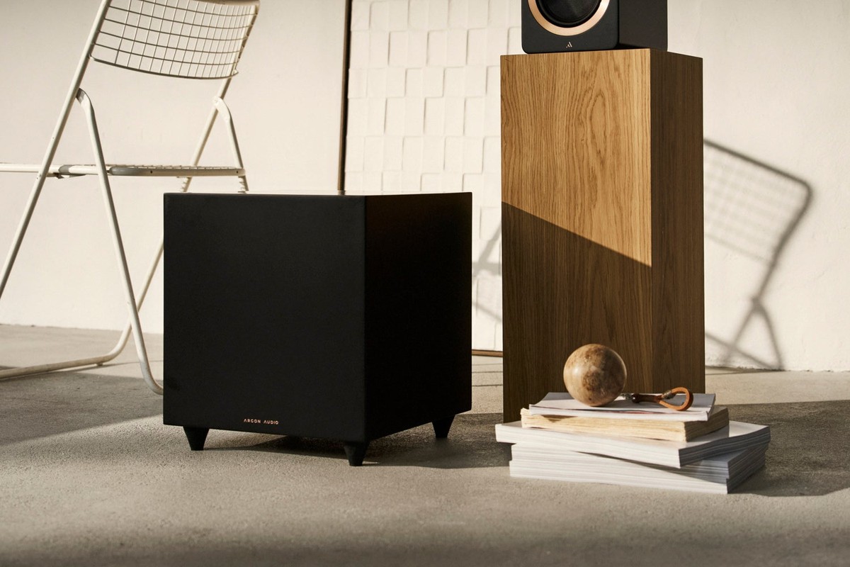Subwoofer nero opaco a terra davanti a un diffusore su una colonna in legno
