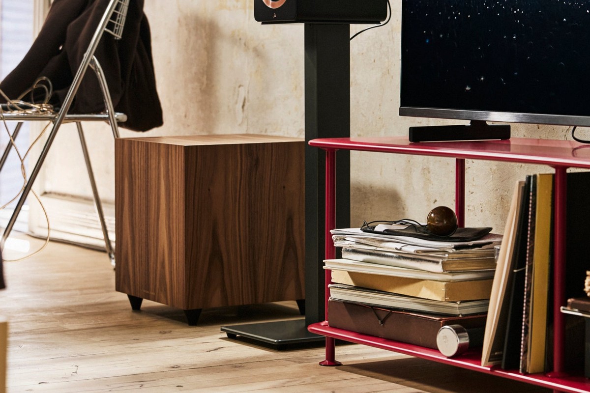 Subwoofer impiallacciato noce sotto un mobile TV rosso, accanto a un diffusore su stand
