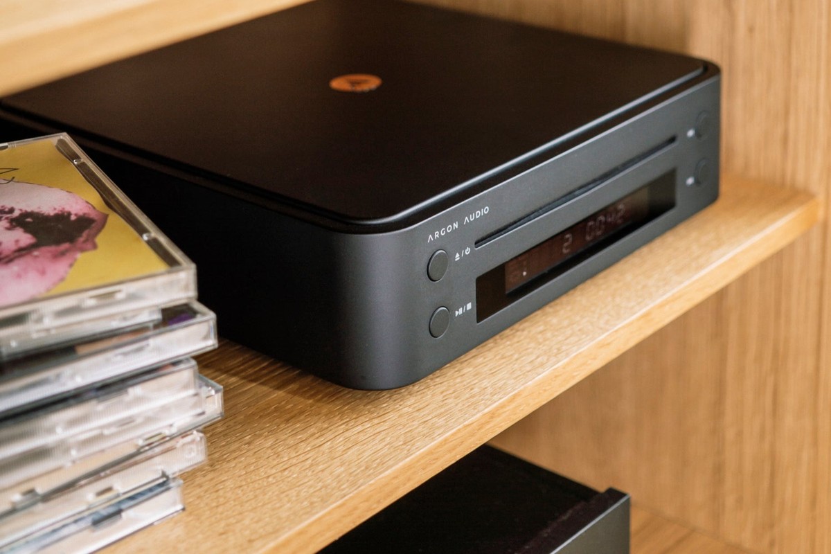 Lettore CD nero su una mensola in legno accanto a una pila di CD