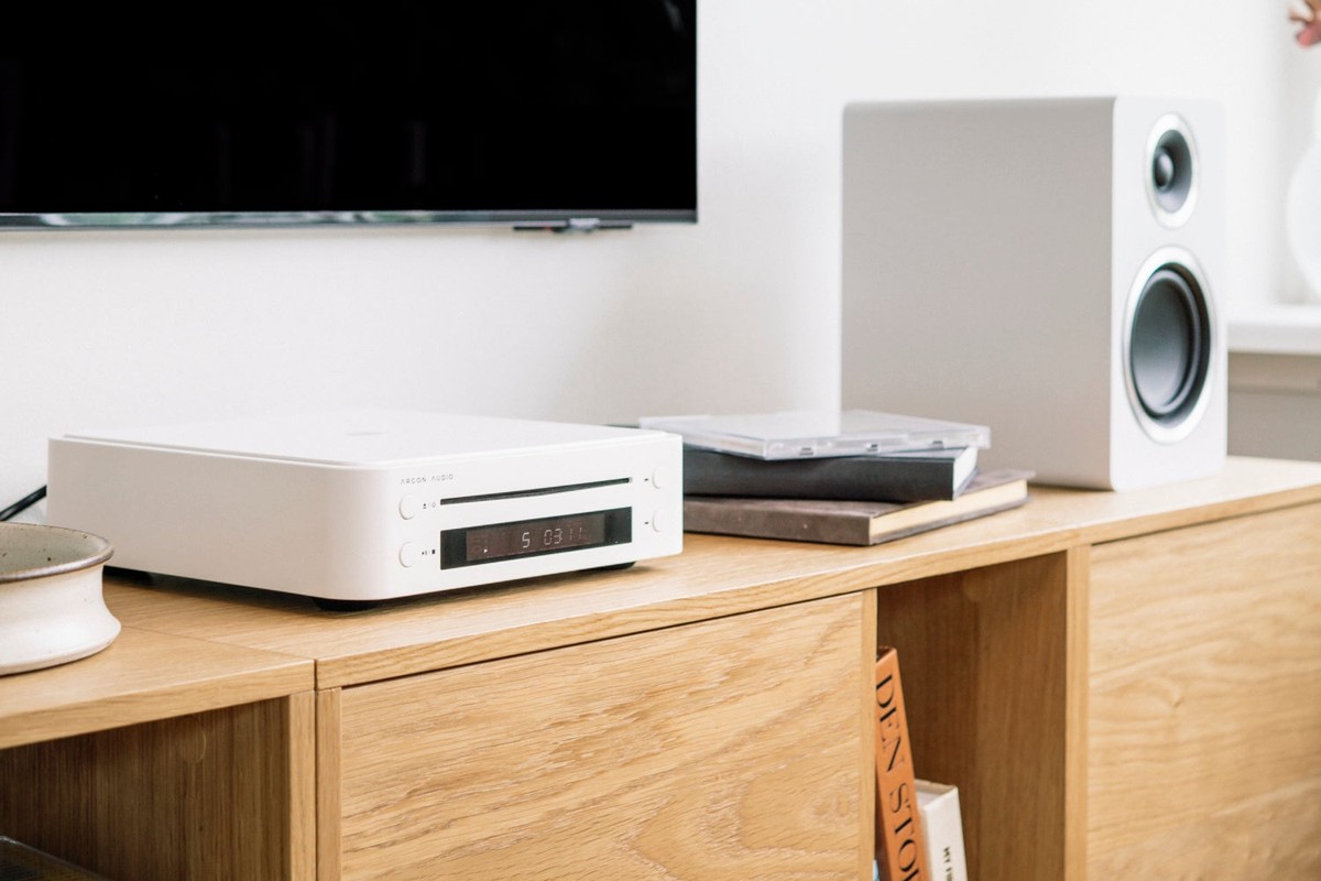 Lettore CD bianco su un mobile TV in legno vicino a un diffusore bianco