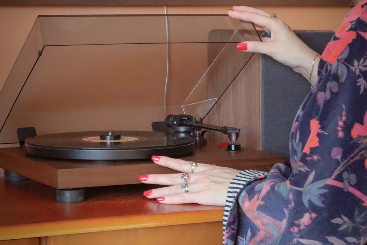 Main qui soulève le capot d'une platine en noyer posée sur un meuble en bois