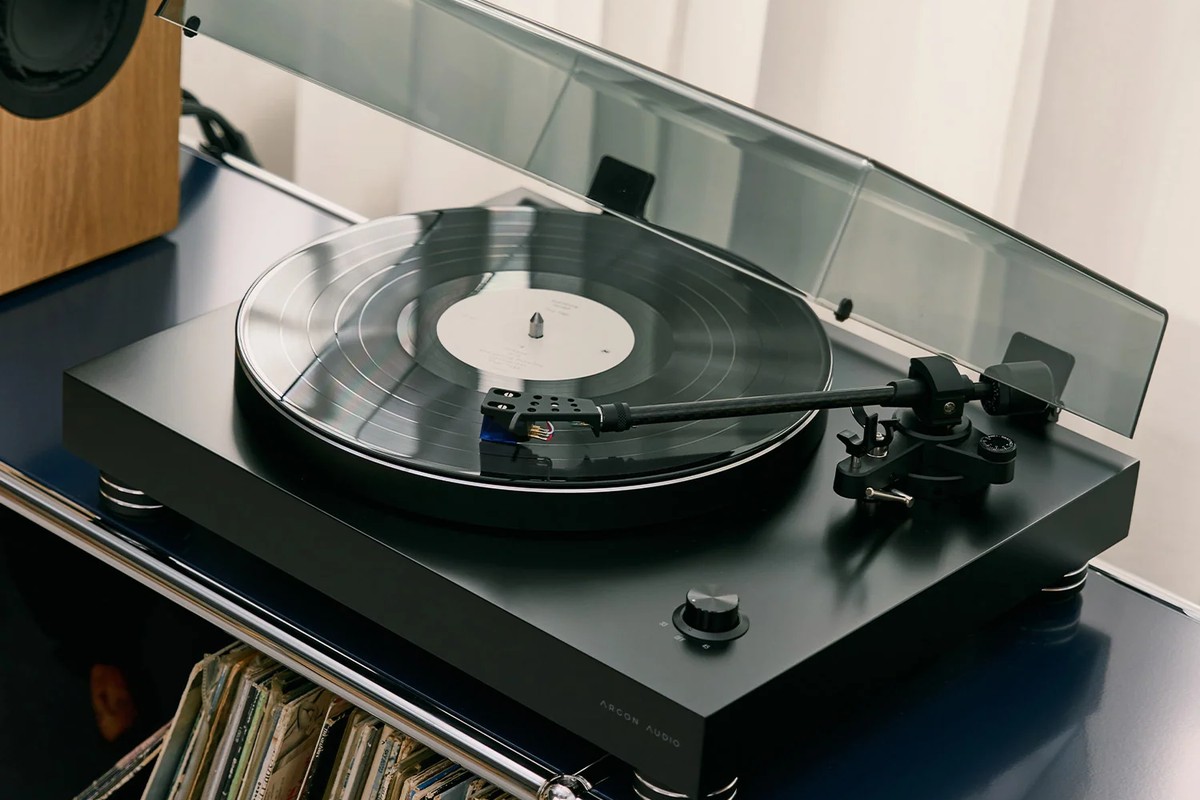 Black turntable with the lid open above a record collection