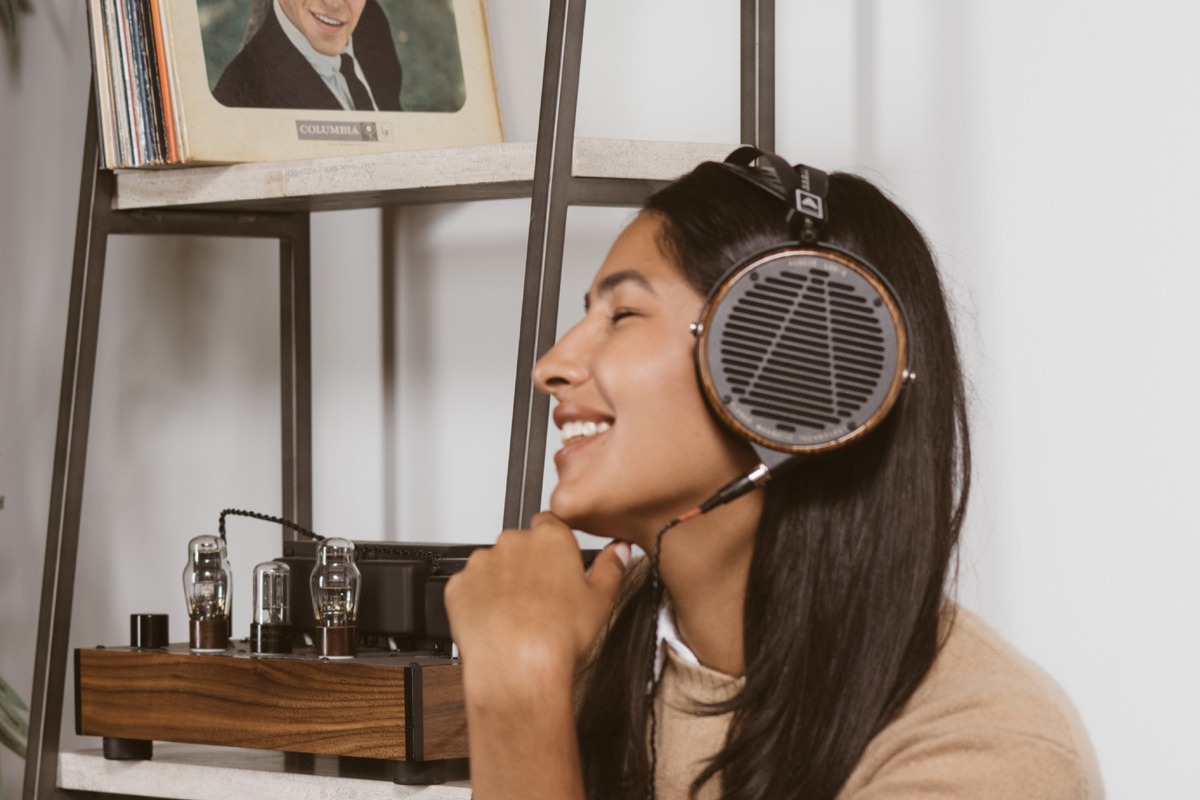 Cuffie indossate da un'utente sorridente, seduta vicino a un mobile hi-fi con amplificatore a valvole e giradischi