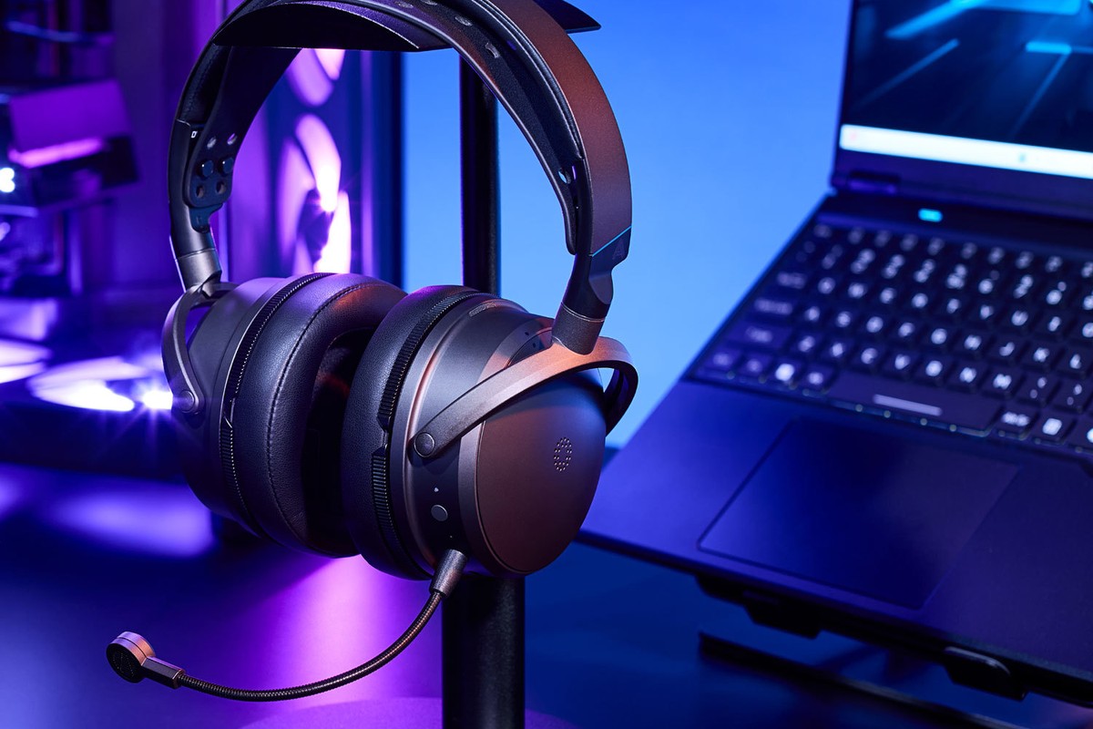 Audeze Maxwell 2 gaming headset for PlayStation, on a stand, gaming setup with a laptop in the background