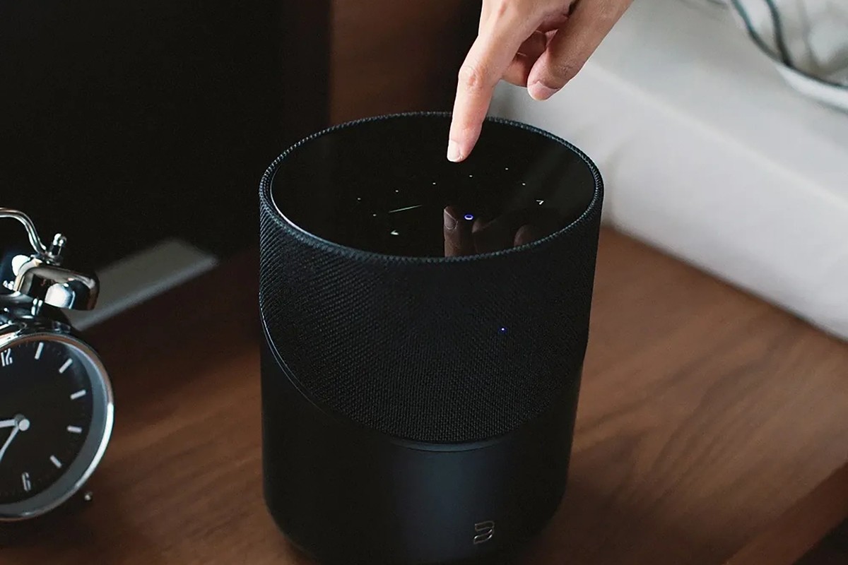 Black cylindrical speaker on a sideboard, a hand touching the top surface
