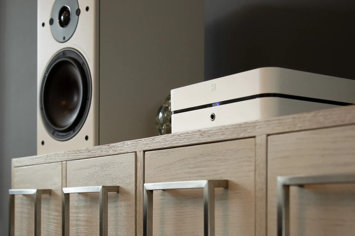 White amplifier on a light sideboard next to a speaker
