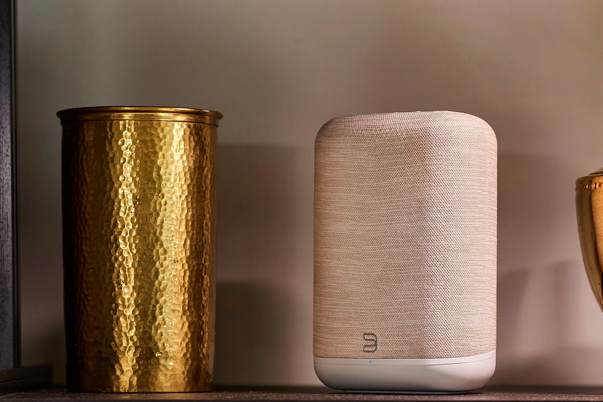Enceinte beige posée sur un meuble à côté d'un vase en laiton