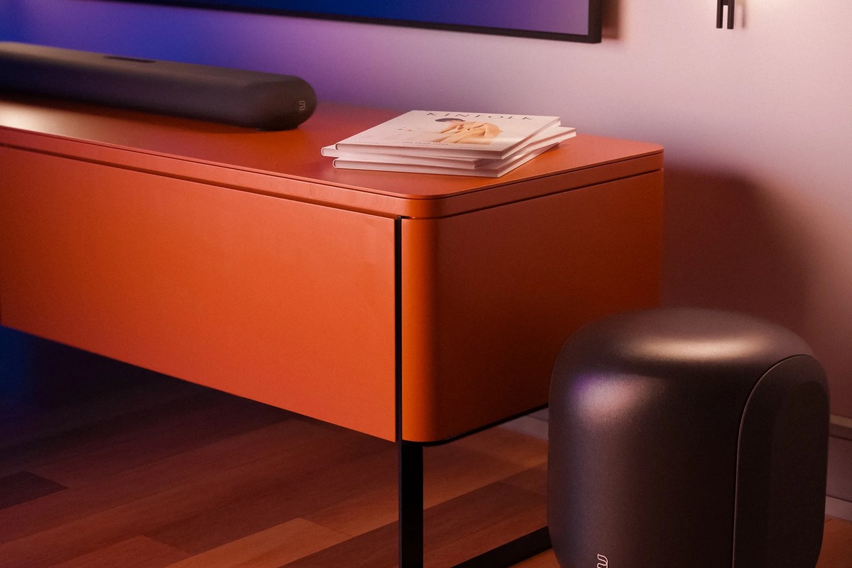 Black subwoofer on the floor near an orange cabinet, screen lit behind