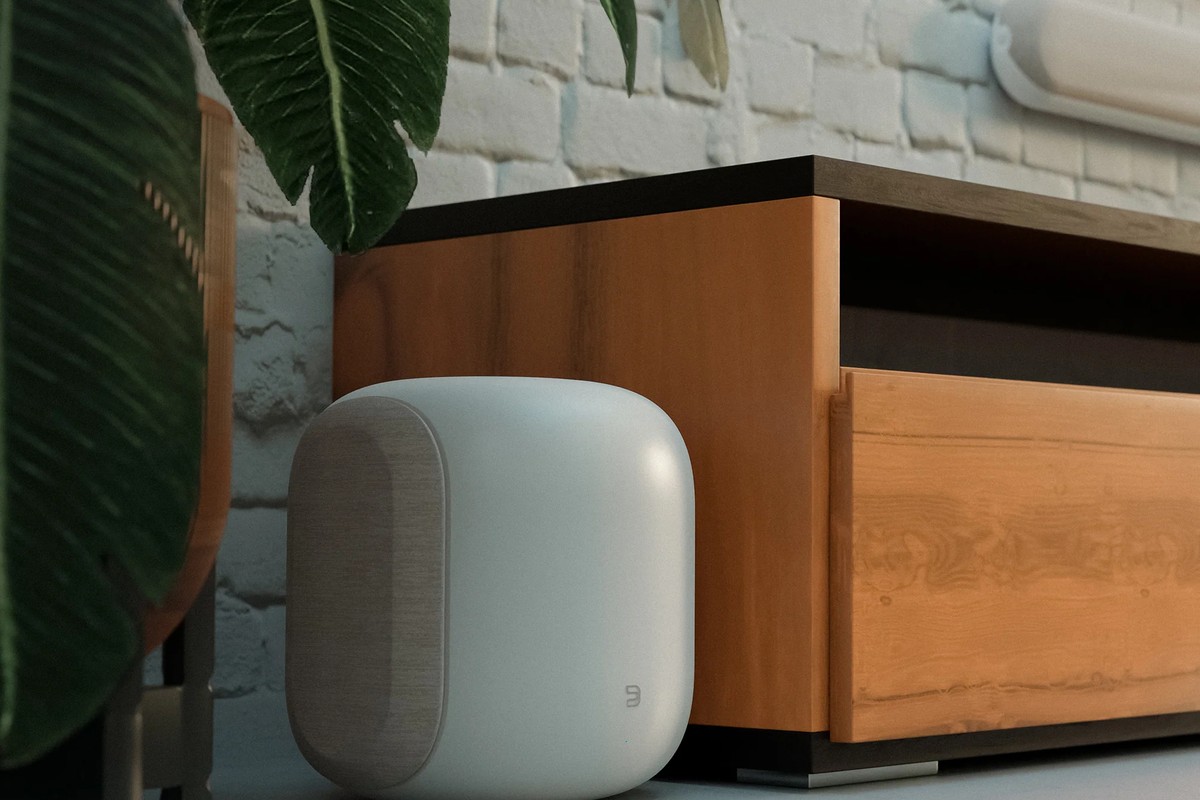 White subwoofer placed near a wooden cabinet, green plant in the foreground