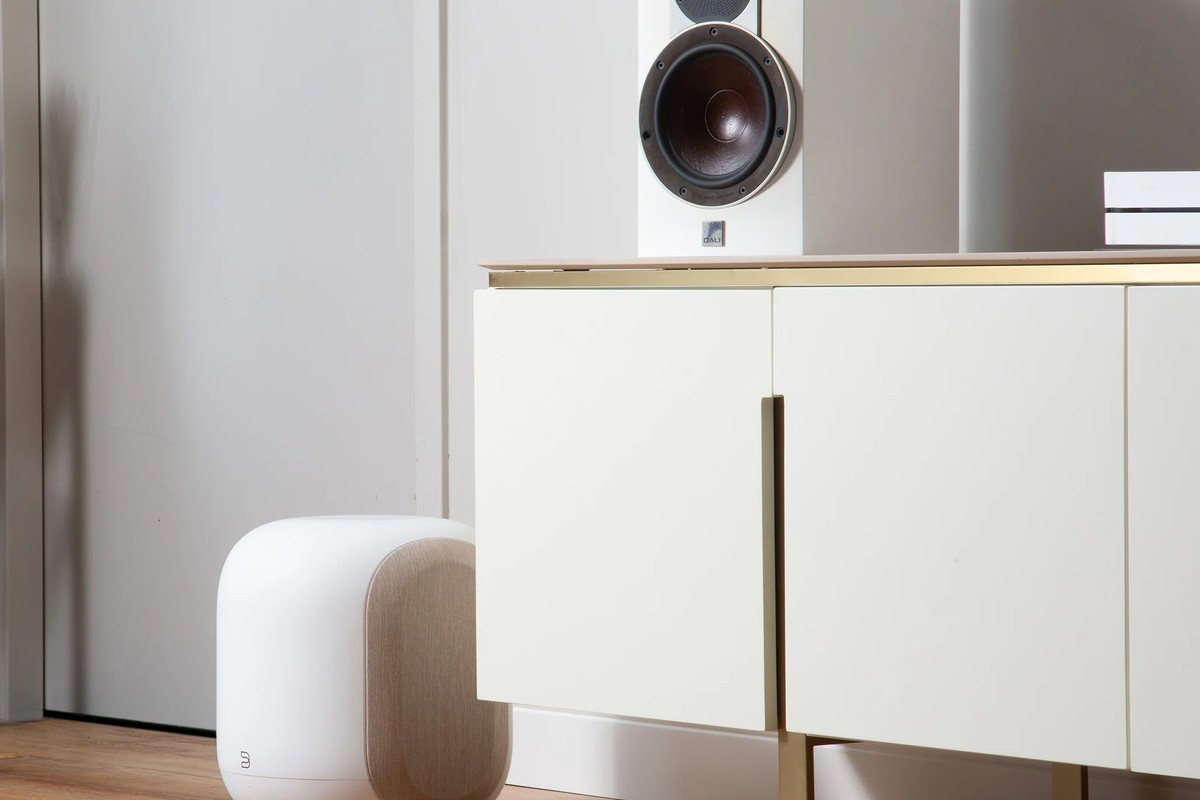 White model on the floor against a light sideboard, speaker above