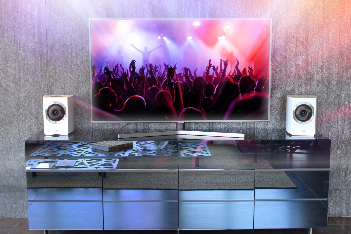 A pair of white speakers framing a television on a lacquered cabinet