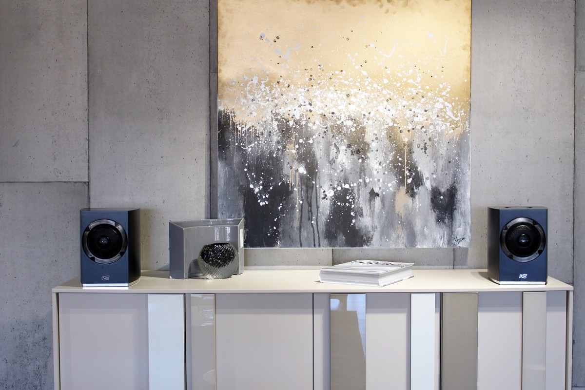 Two black speakers on a pale console below a large abstract canvas