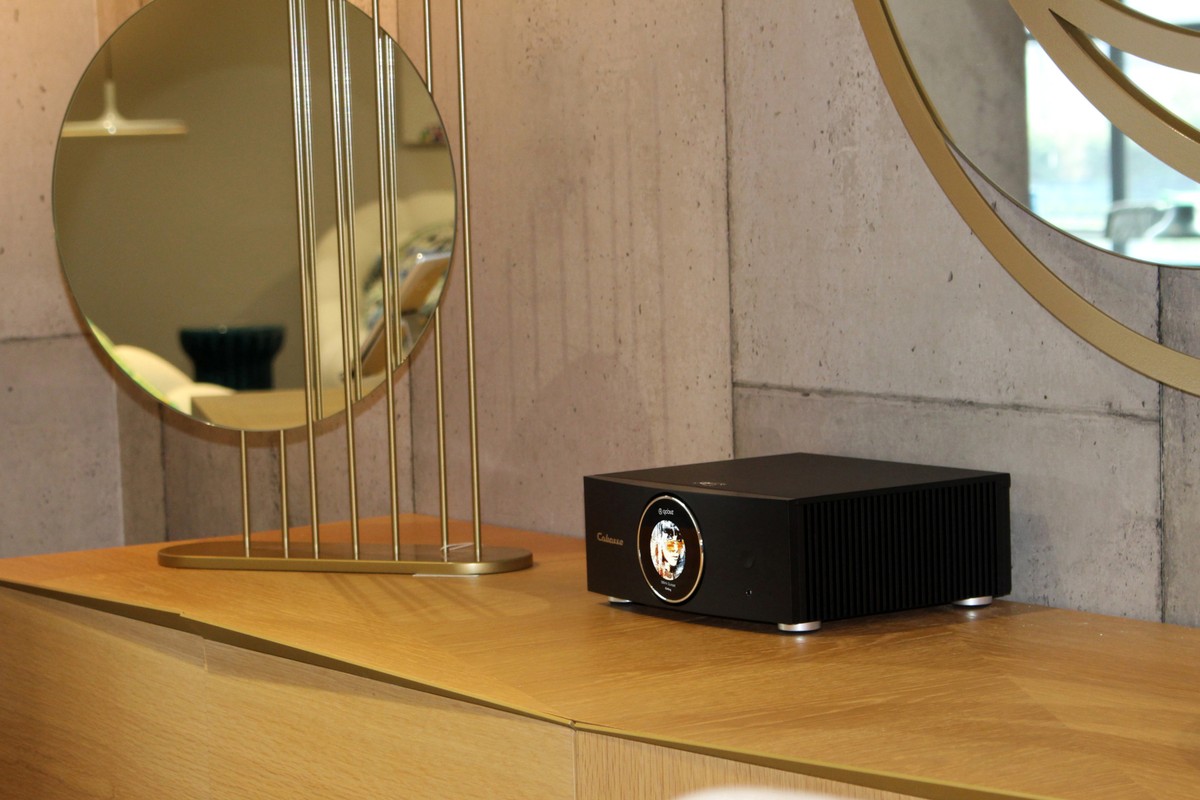 Amplificateur noir sur un plan en chêne, devant un miroir rond doré