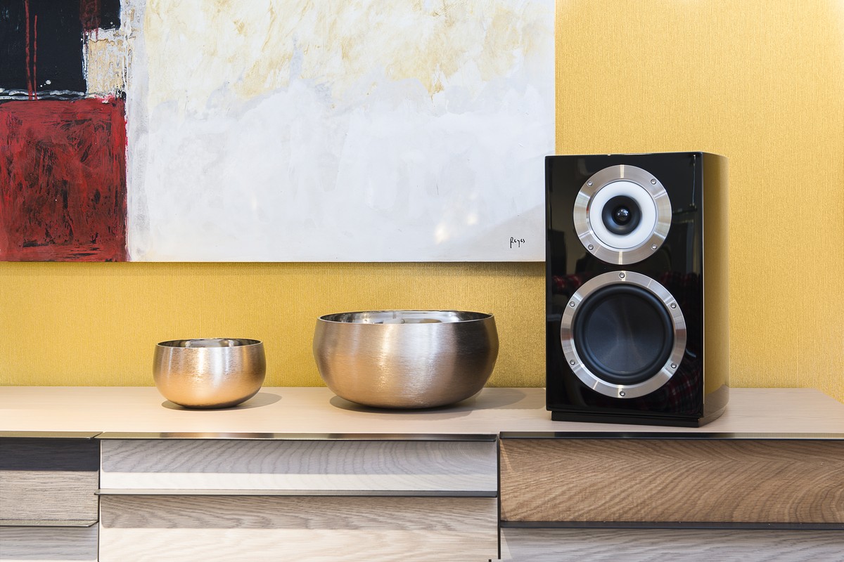 Enceinte laquée noire sur un meuble bas, coupes en métal et toile abstraite au mur