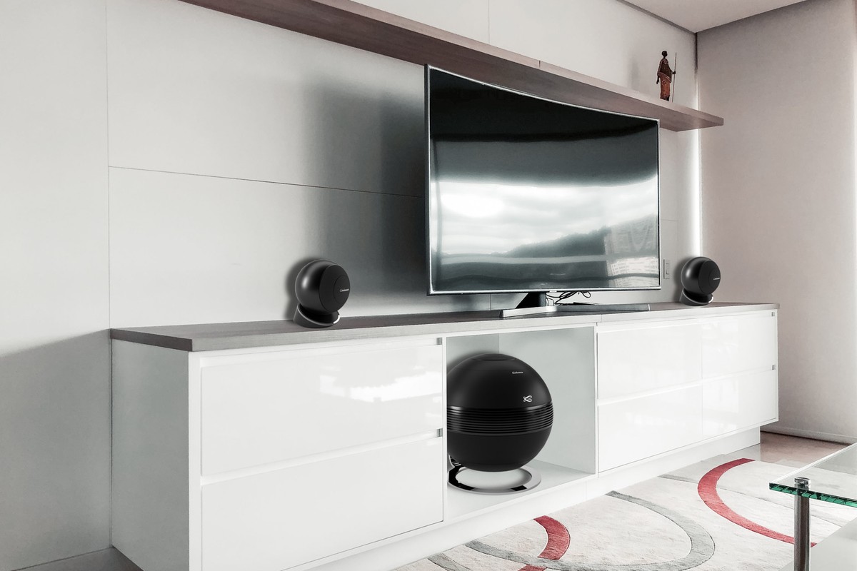 Due satelliti iO3 ai lati di un televisore, subwoofer sferico sotto il mobile