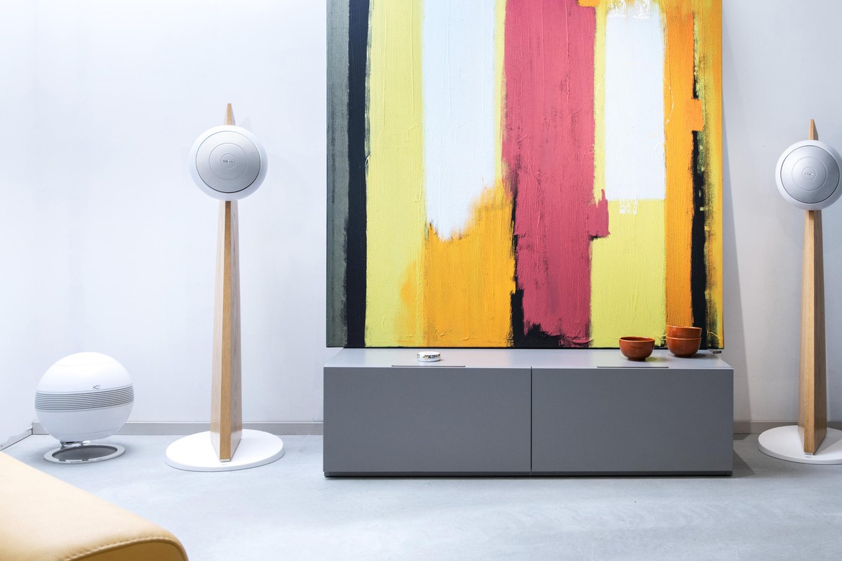 Due diffusori su colonne di rovere ai due lati di una consolle grigia, davanti a una tela colorata