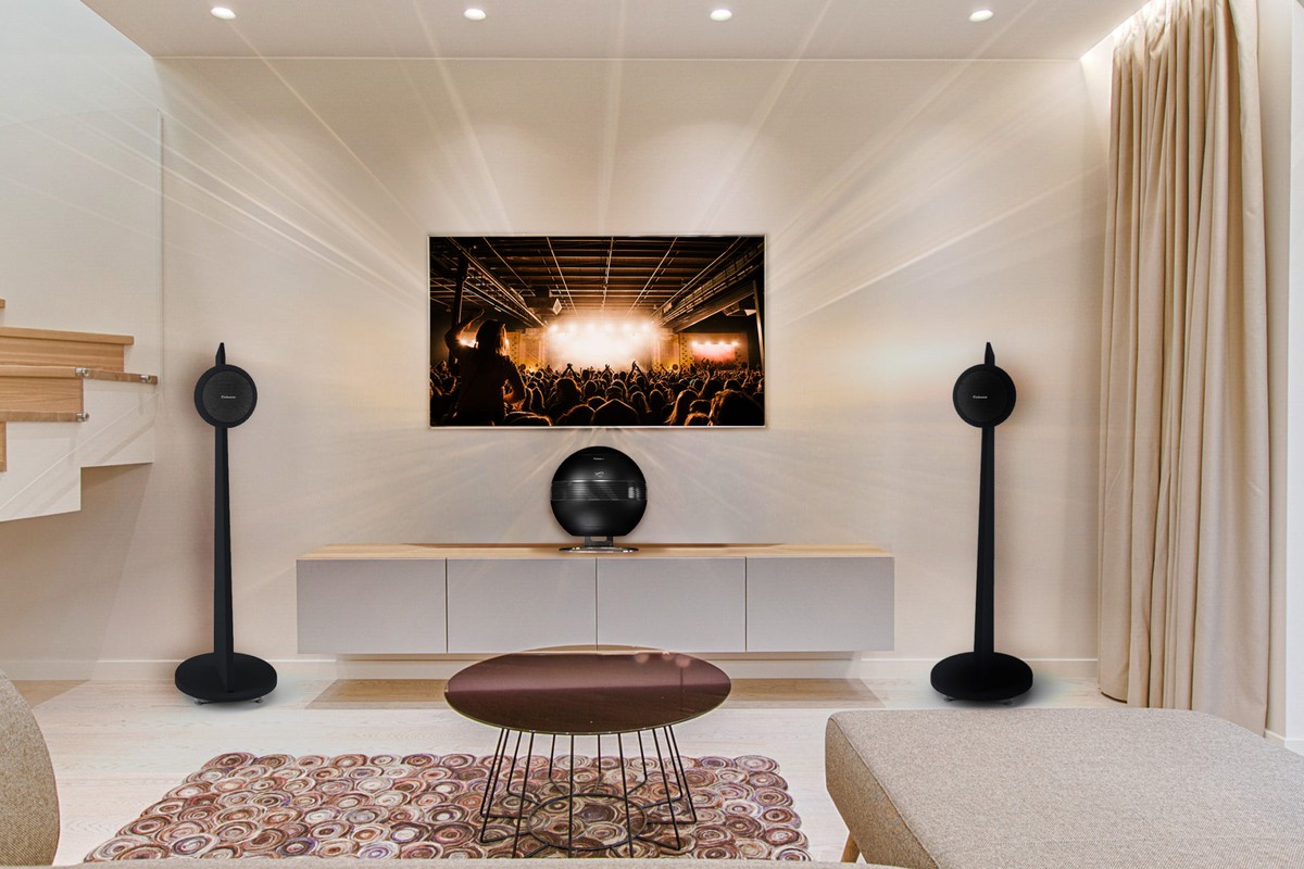 Soggiorno con schermo a parete, due Riga 2 su piedistalli neri ai lati, subwoofer sulla credenza