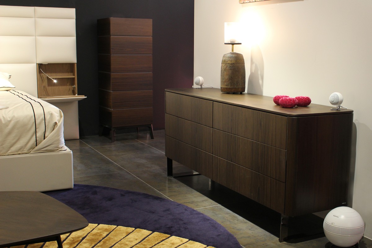 Schlafzimmer mit Kommode aus dunklem Holz, weisse Satelliten und Subwoofer am Boden