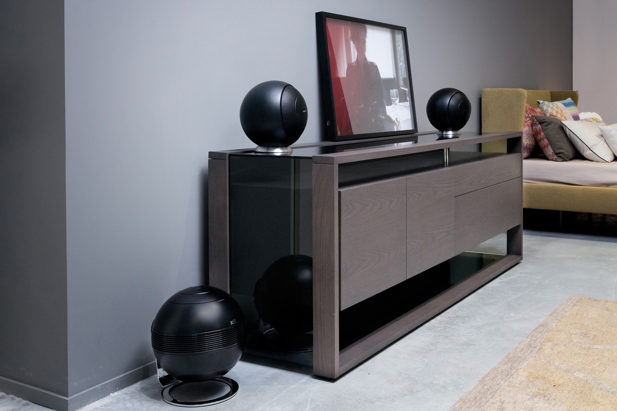 Black subwoofer on the floor in front of a sideboard, two spherical speakers on top