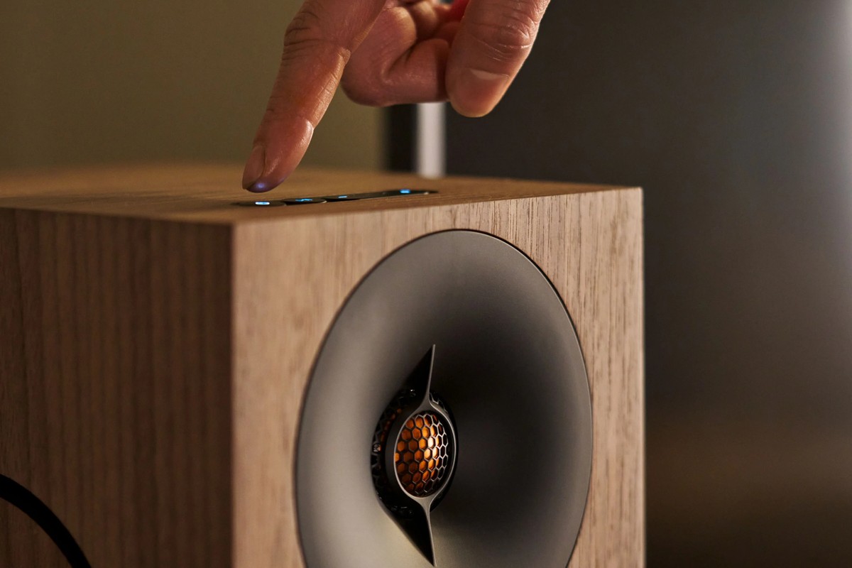 Doigt appuyant sur les touches du dessus d'une enceinte en noyer, tweeter à pavillon au premier plan