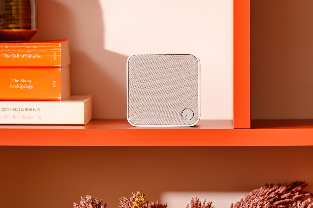 White speaker on an orange shelf next to a pile of books