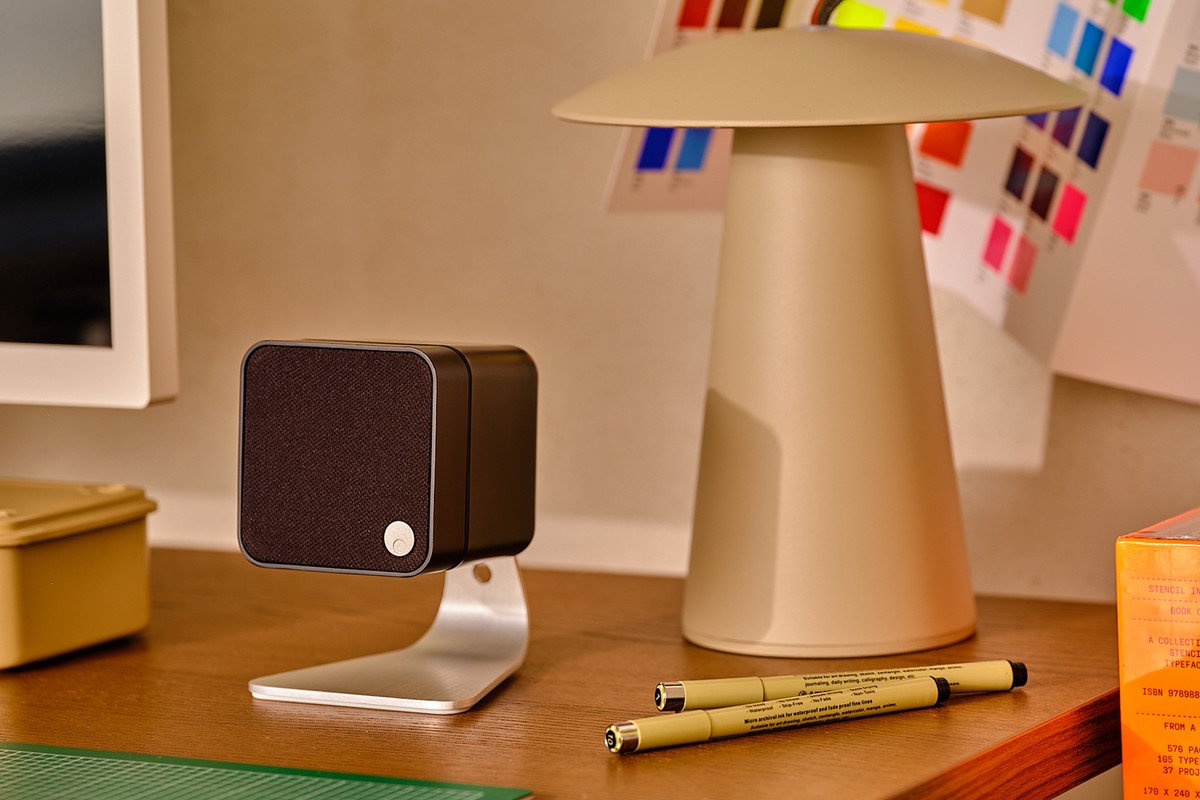 Black MSX 10 speaker on a stand placed on a desk, next to a lamp and pens