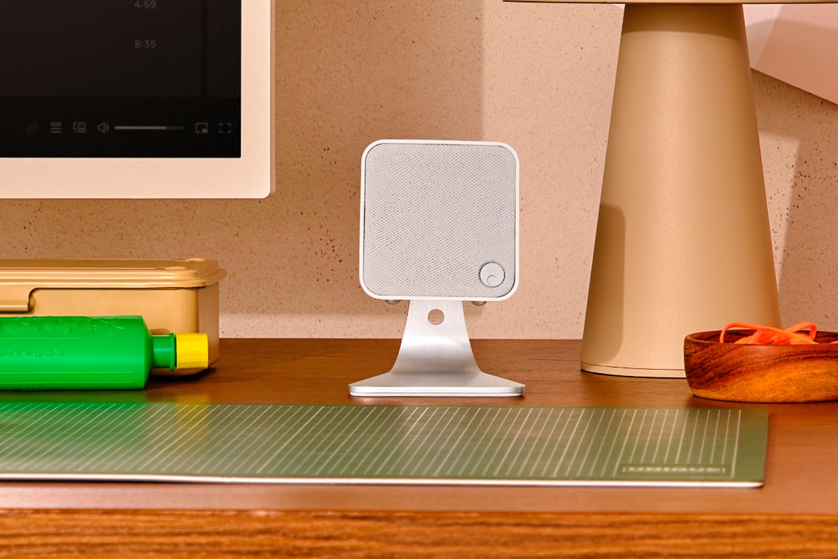 White speaker on a stand in front of a screen, on a work desk
