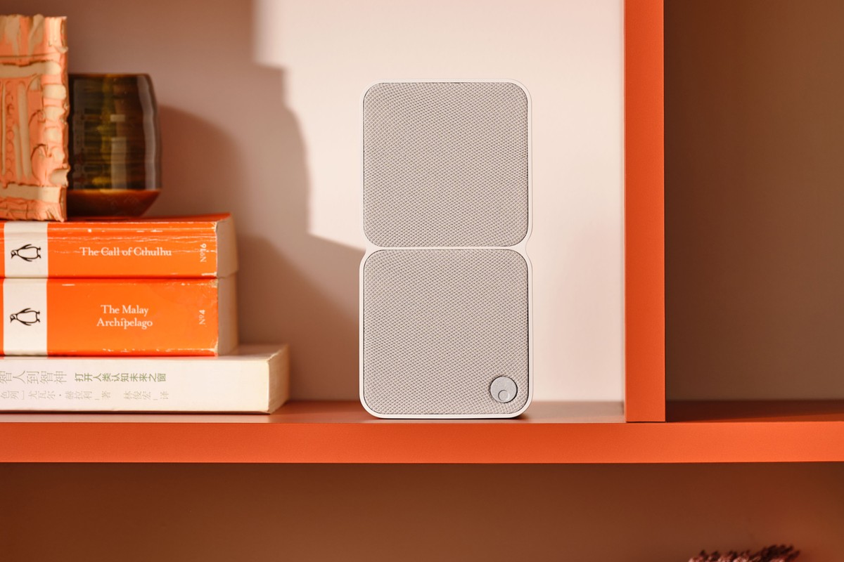 White satellite speaker on an orange shelf between books