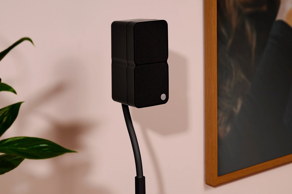 Black satellite speaker on a stand beside a wall frame