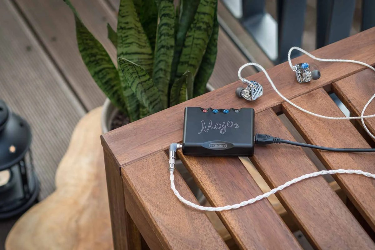 Chord Mojo 2 auf einem Terrassentisch neben In-Ear-Hörern