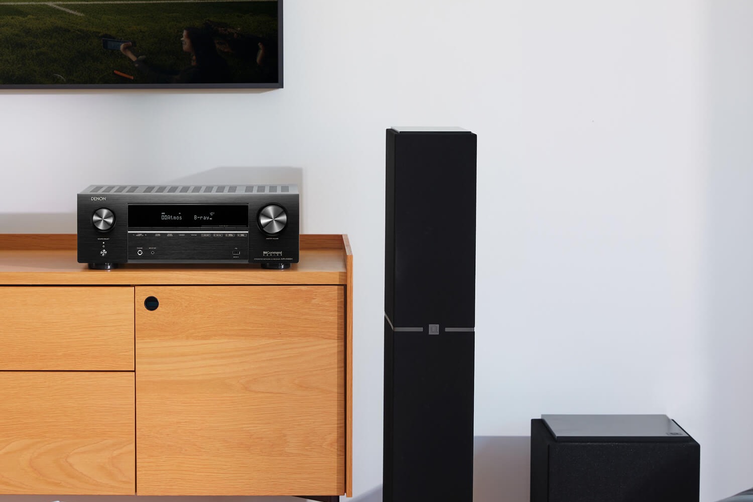 Ampli-tuner noir sur un buffet en bois clair, enceinte colonne et caisson de basses
