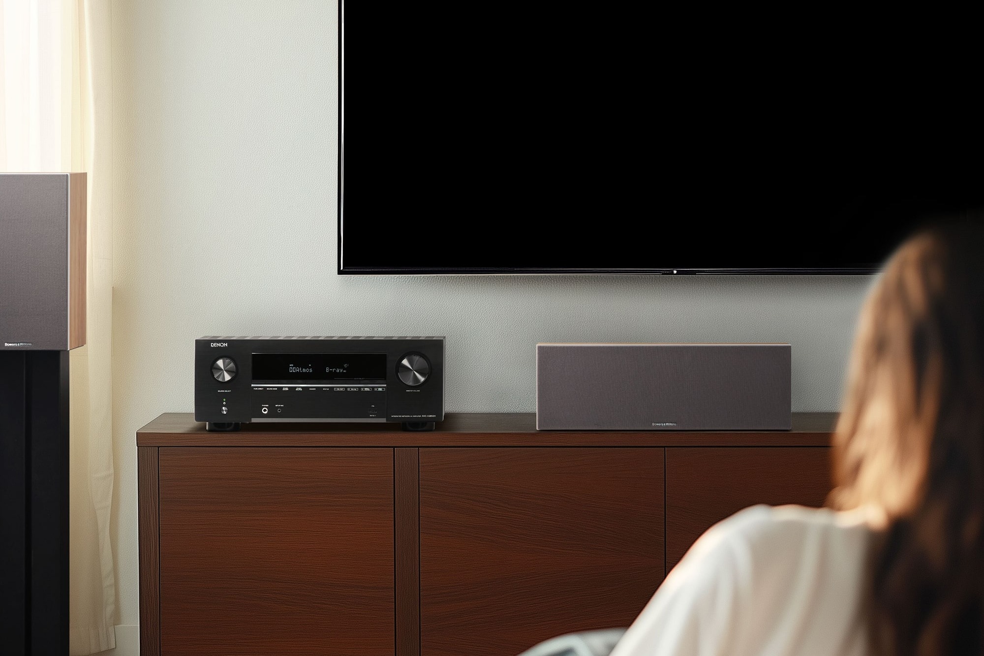 Viewer in front of a large TV, AV amplifier and centre speaker on the cabinet