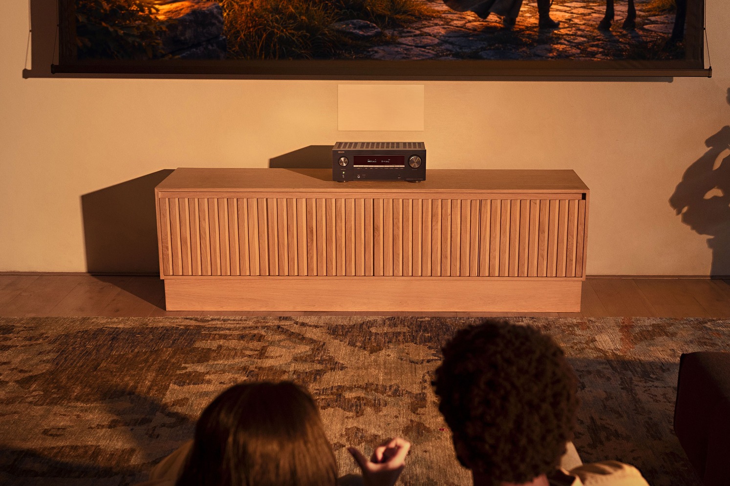 Two viewers facing a projection screen, AV amplifier on a low cabinet