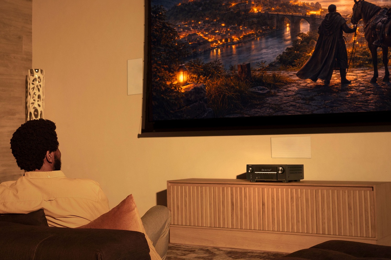 Viewer on a sofa, AV amplifier on a wooden cabinet below the screen
