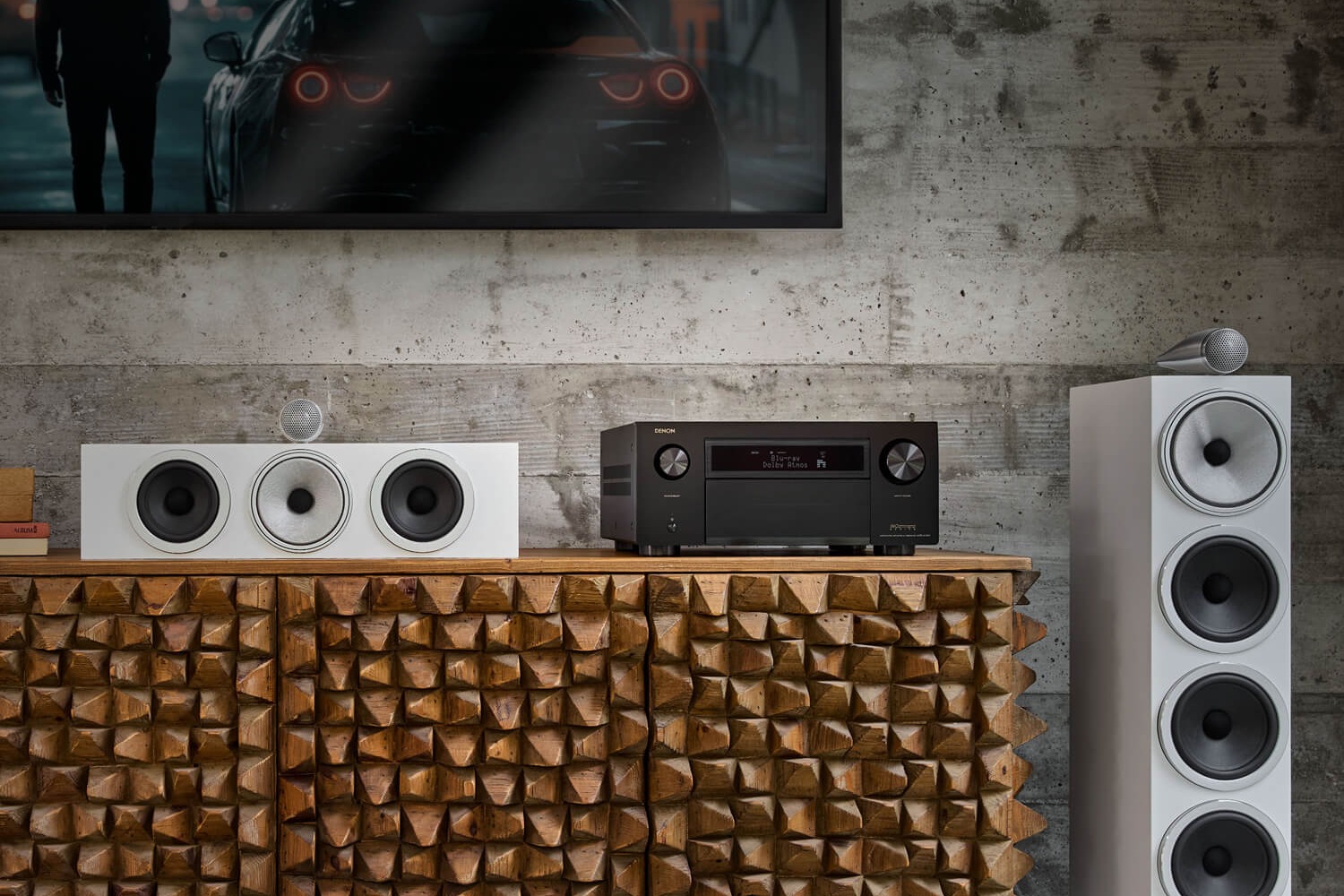 Amplificateur AV noir sur un buffet sculpté, enceinte centrale et colonne blanches