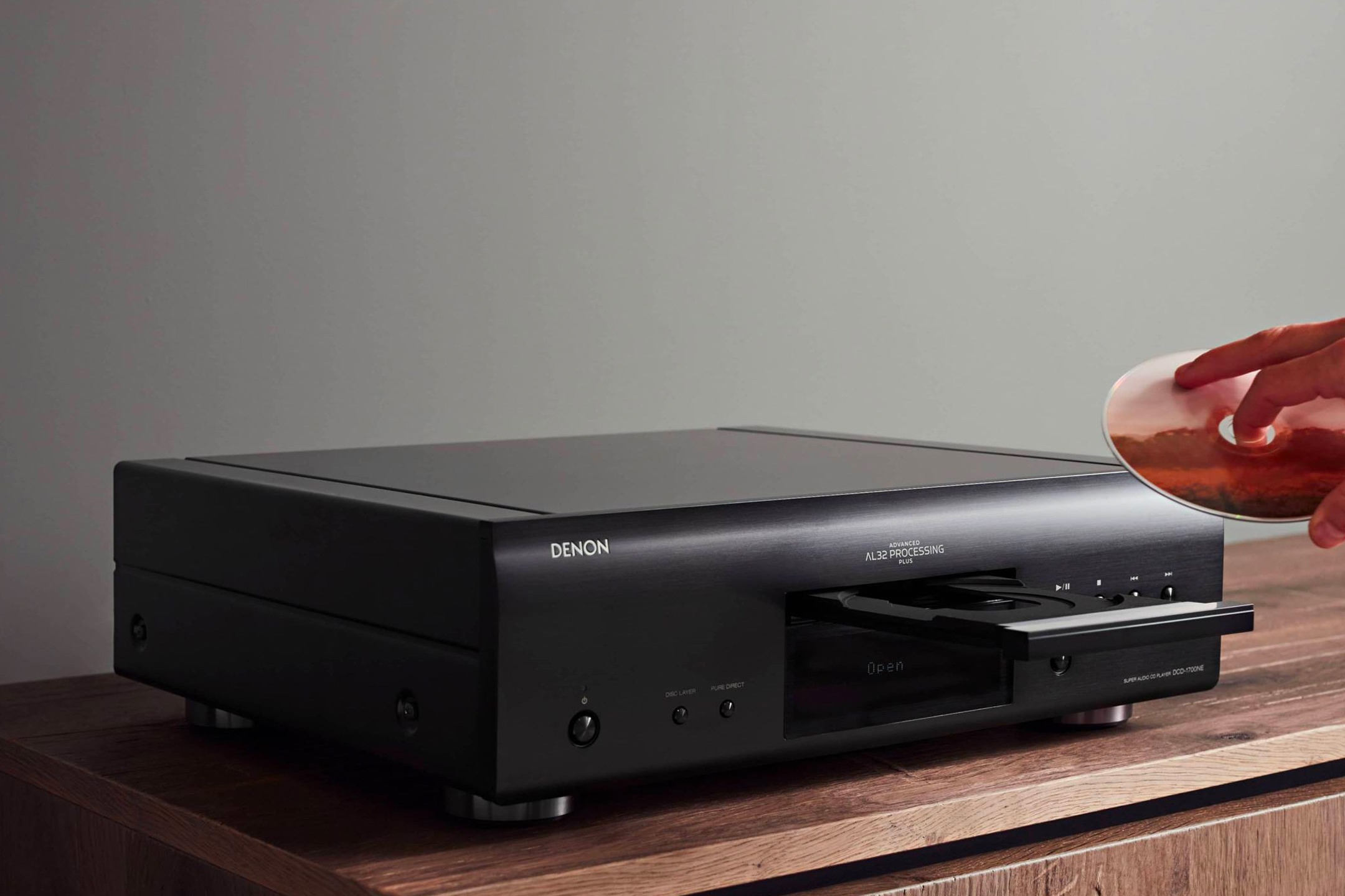Main insérant un CD dans un lecteur hi-fi posé sur un meuble