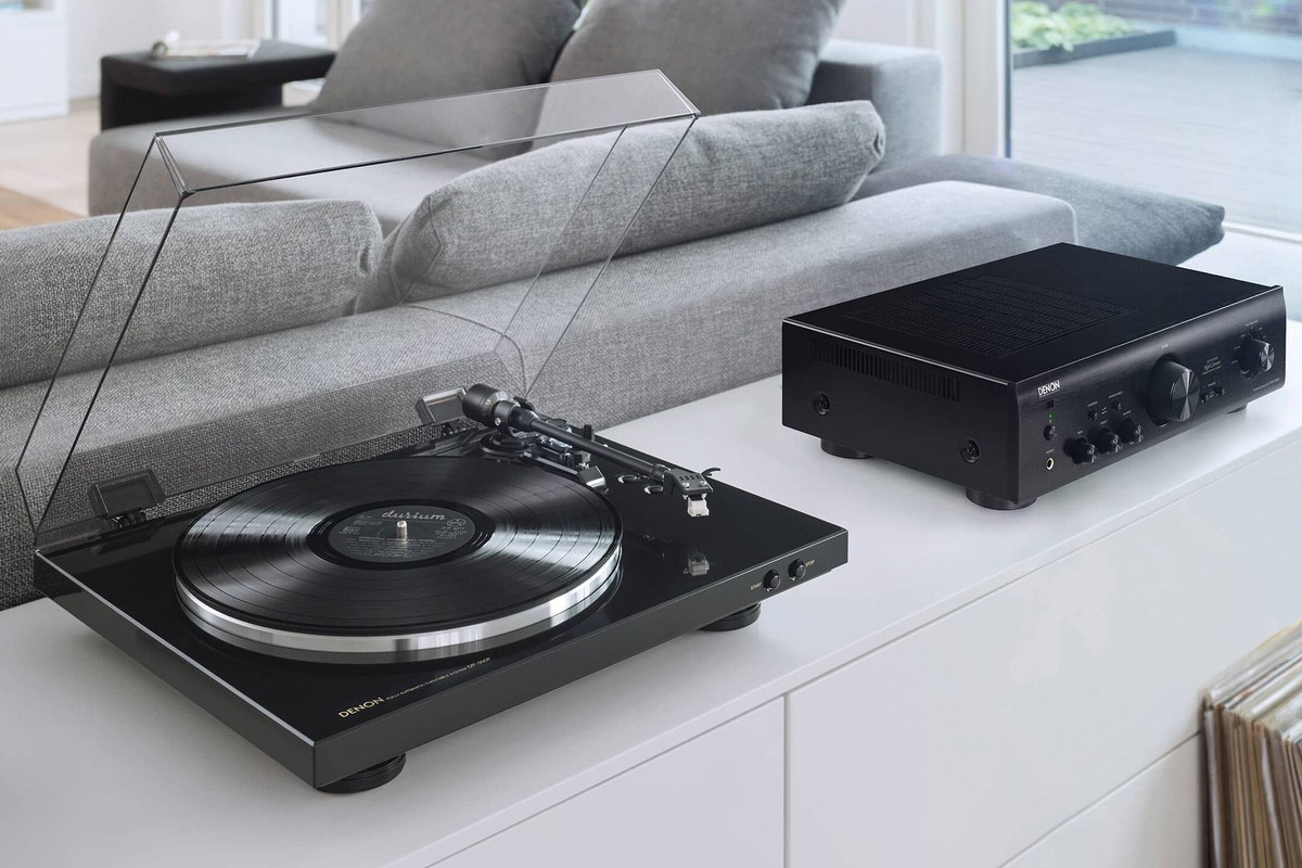 Giradischi nero con coperchio e disco su una credenza bianca, accanto a un amplificatore
