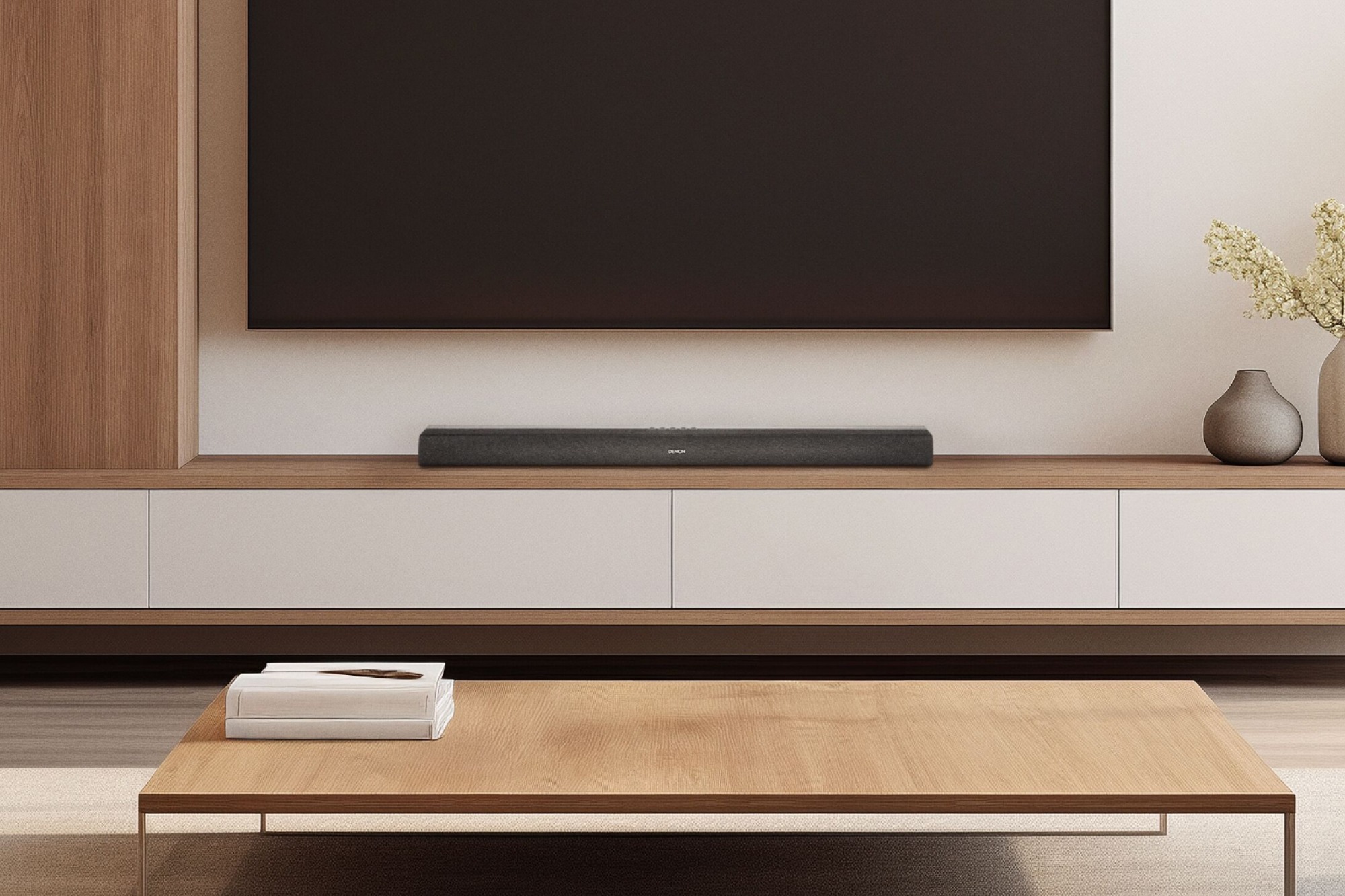 Barre de son Denon DHT-S218 sur un meuble TV blanc, sous un grand téléviseur mural