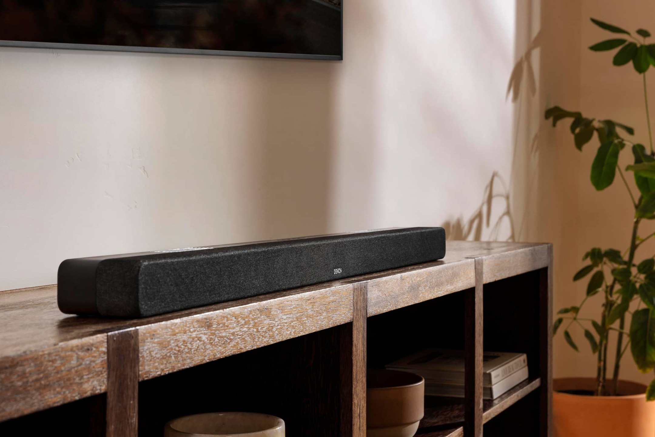 Soundbar on a wooden console beneath a TV, natural light