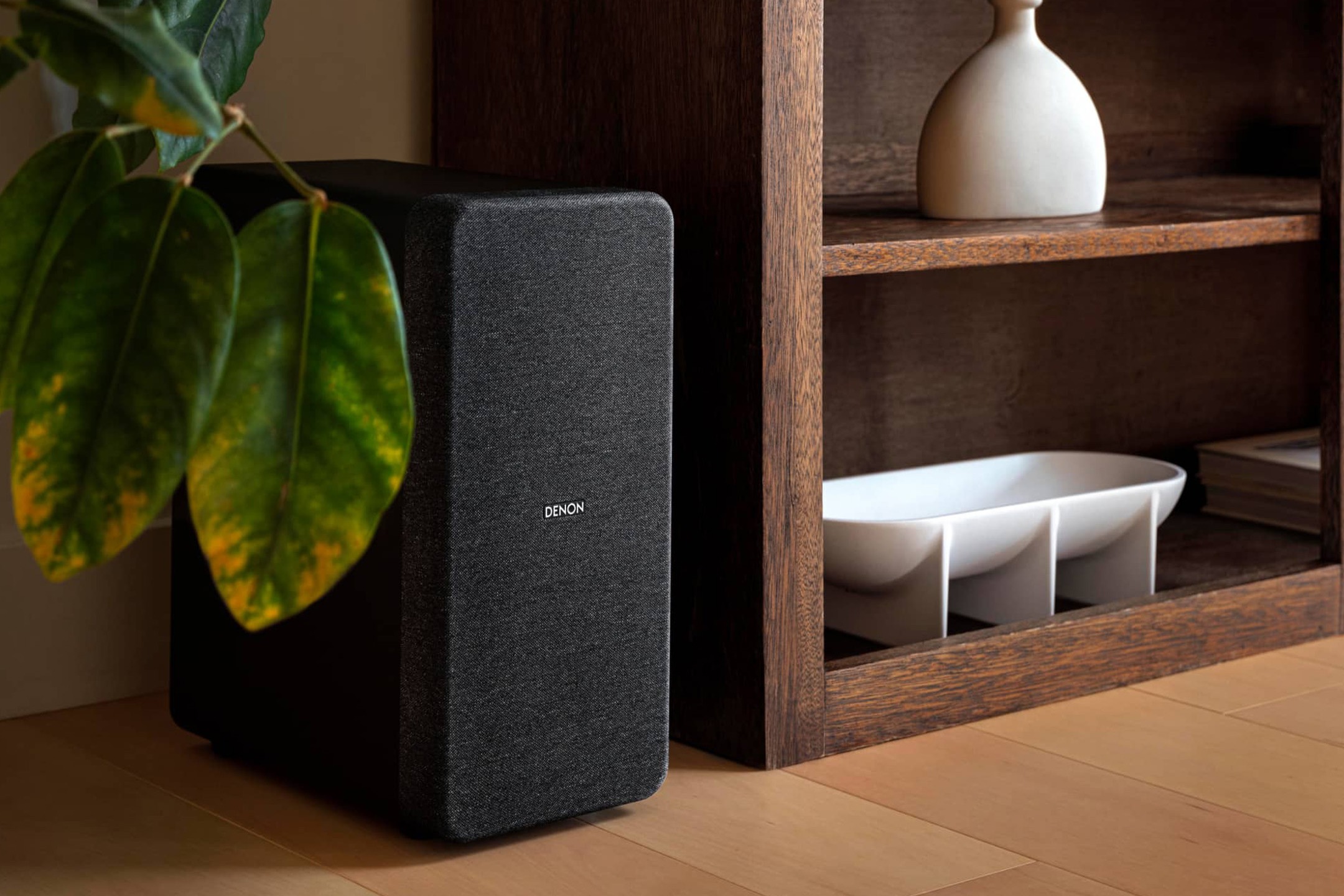 Black wireless subwoofer on the floor next to a wooden shelf unit