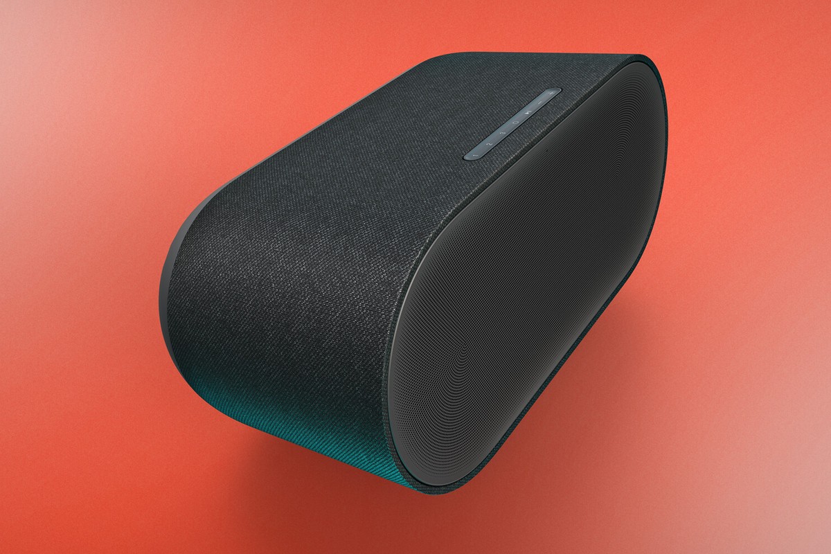 Grande enceinte sans fil gris anthracite vue de trois quarts, sur fond corail